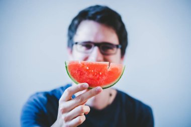 Gözlüklü yakışıklı genç adam karpuz yiyor.