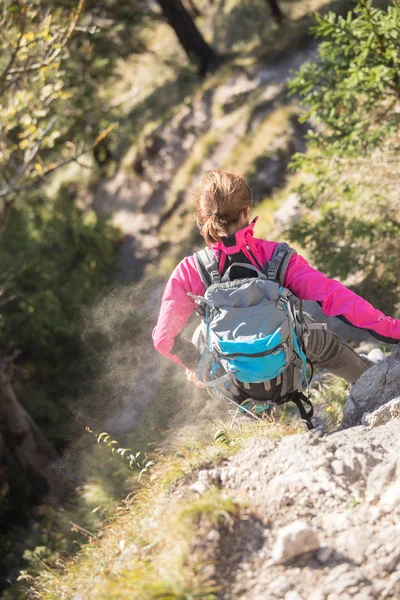 年轻的女徒步旅行者爬上山顶悬崖上的岩石 — 图库照片