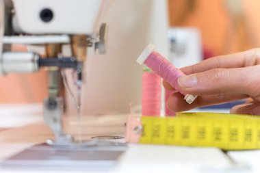 Bir terzi atölyesinde pembe bir iplik tutan bir kadın eli.
