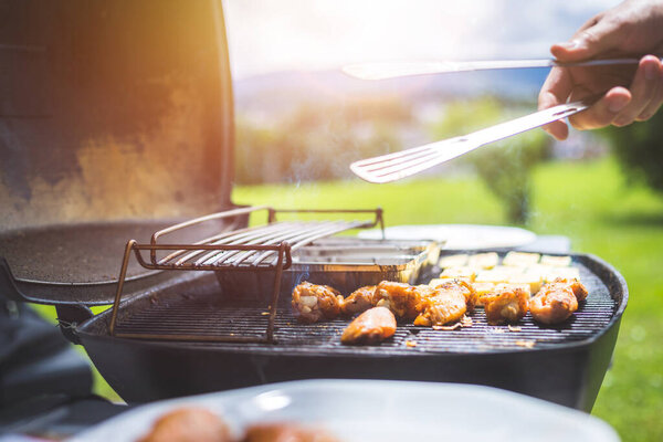 Close up of chicken wings, cheese and vegetables on gas grill. Summer time, outdoors.