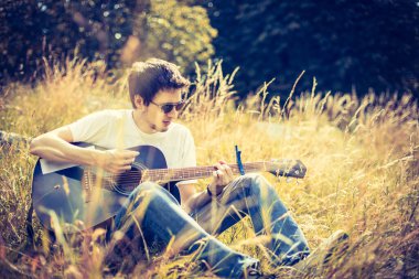 Genç adam bir nehirde oturuyor ve batı gitarını çalıyor.