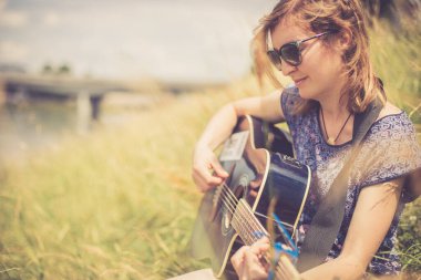 Güzel genç kız bir nehirde oturuyor ve batı gitarını çalıyor.