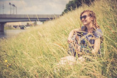 Güzel genç kız bir nehirde oturuyor ve batı gitarını çalıyor.