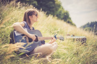 Güzel genç kız bir nehirde oturuyor ve batı gitarını çalıyor.