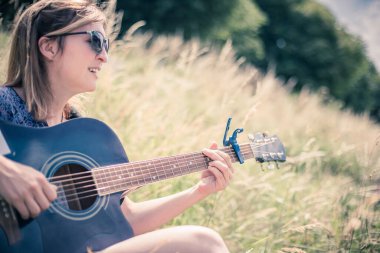 Güzel genç kız bir nehirde oturuyor ve batı gitarını çalıyor.