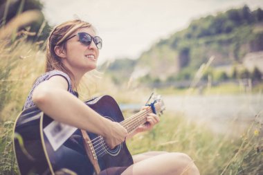 Güzel genç kız bir nehirde oturuyor ve batı gitarını çalıyor.