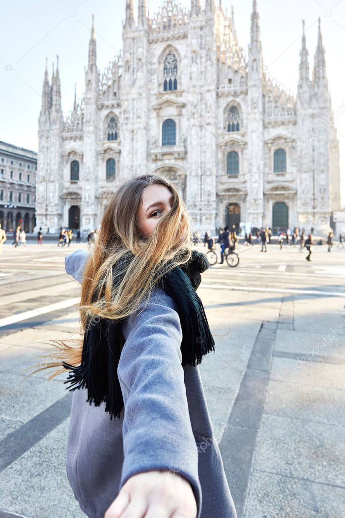 Travel girl smile back while pulling hand in front of Duomo of Milan Italy during day