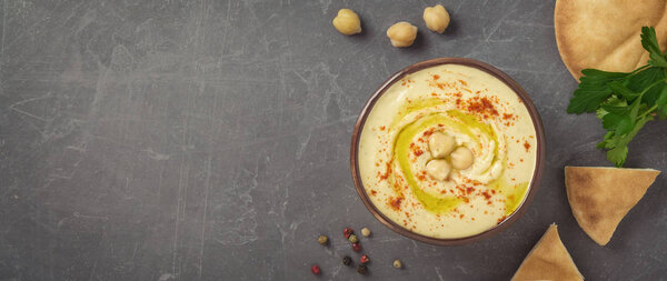 Chickpea hummus in a bowl, chickpeas, parsley, pepper and pita bread on grey background. Top view, copy space.