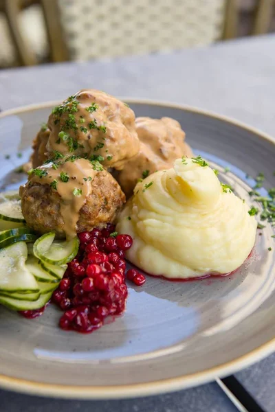 Delicious meat balls and mashed potato with pickled cucumber Swedish style on a grey plate, vertical shot
