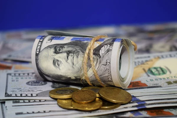 Um rolo de dólares no fundo de notas de cem dólares espalhadas e várias moedas — Fotografia de Stock
