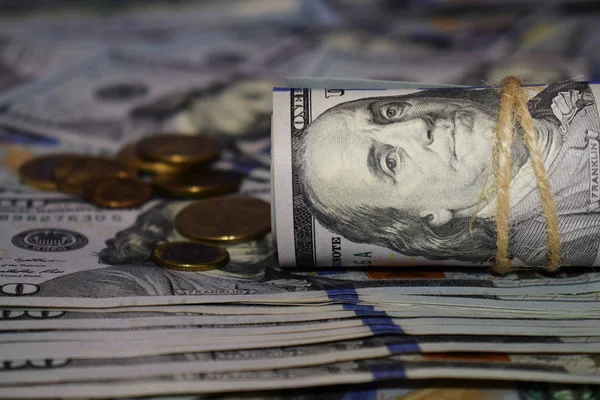 Рулон долларов на фоне разбросанных стодолларовых купюр и различных монет — стоковое фото