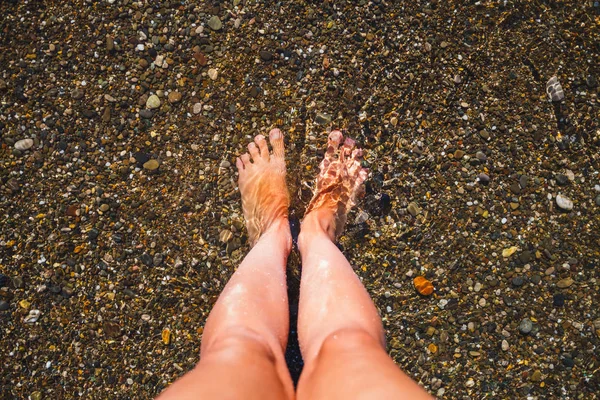 Women\'s feet splashing in sea clear water on tropical beach.