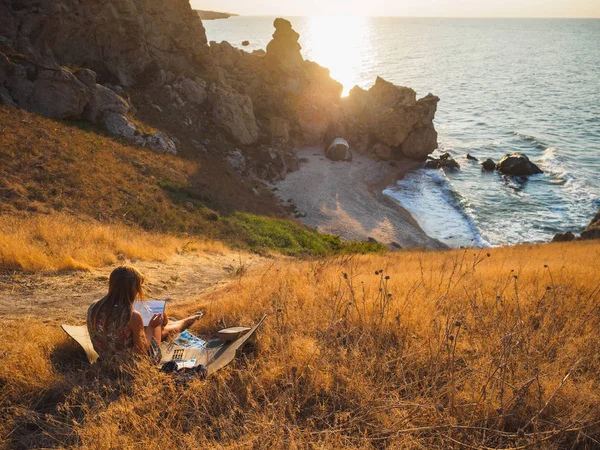 The artist draws the sea, Rus sea bay. Downstairs is her tent. She lives in a tent by the sea in a shell bay. Wakes up in the morning and sees the sea. Here you can sometimes see dolphins.