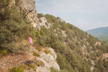 Kız bir kaya üzerinde oturuyor. Nehir ishal. Kayalar ve kron ağaçların