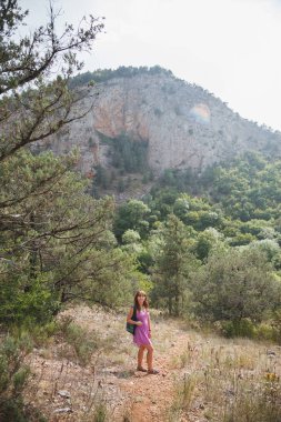 Kız bir kaya üzerinde oturuyor. Nehir ishal. Kayalar ve kron ağaçların