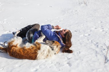 Kız ve Rus tazı karda yuvarlanmak.