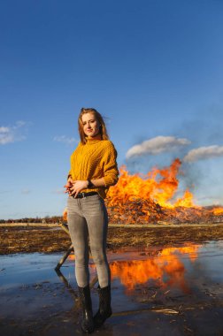 Bir kız sarı kazaklı bir kısa saç kesimi ile büyük bir şenlik ateşi arka plan üzerinde duruyor