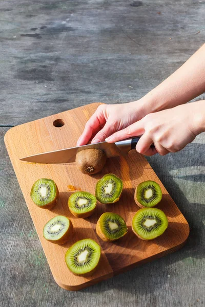 Le mani femminili tagliano il kiwi su un tagliere su sfondo grigio vintage — Foto Stock