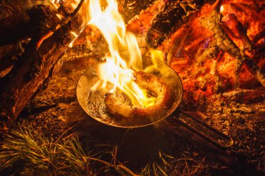 Bir tavada gece ormanda bir yangın sosis ekleme