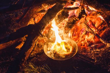 Bir tavada gece ormanda bir yangın sosis ekleme