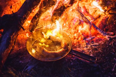 Bir tavada gece ormanda bir yangın sosis ekleme