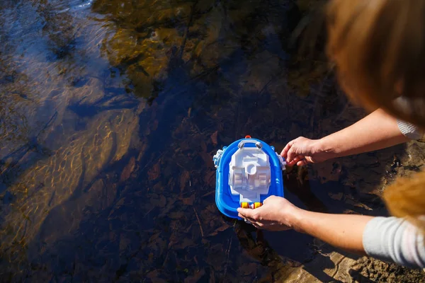 Girl launches a toy boat in the forest creek — Stock Photo, Image