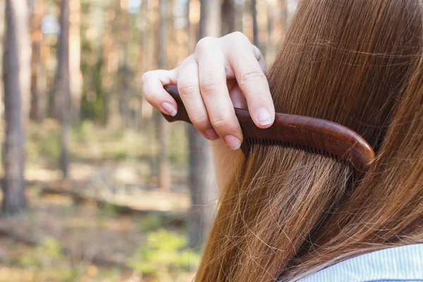 Flicka kamma håret med en träkam i skogen — Stockfoto