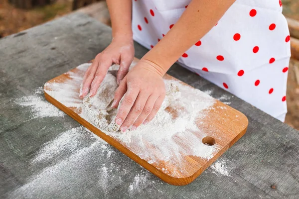 La chica en un delantal blanco prepara la masa en una tabla de cortar — Foto de Stock