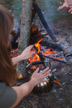 Kız ateşin yanında su ısıtıcısı üzerinde ellerini ısıtır