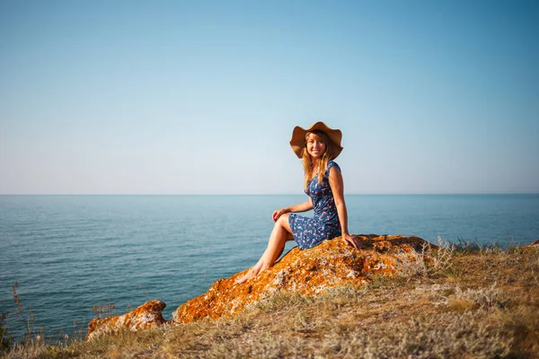 Chica joven con un sombrero en una piedra junto al mar en un día soleado — Foto de Stock