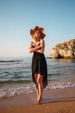 Sahilde siyah elbise ve şapkalı bir kızın portresi