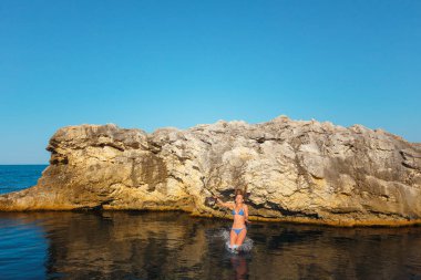 Mavi mayogiyen ve kamerası olan bir kız uçurumdan denize atlar.