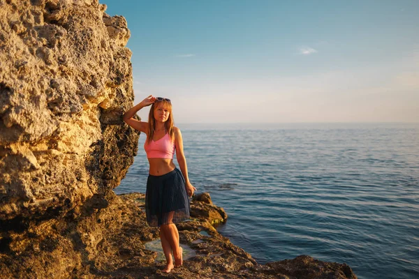 Chica en las rocas en el mar al atardecer — Foto de Stock