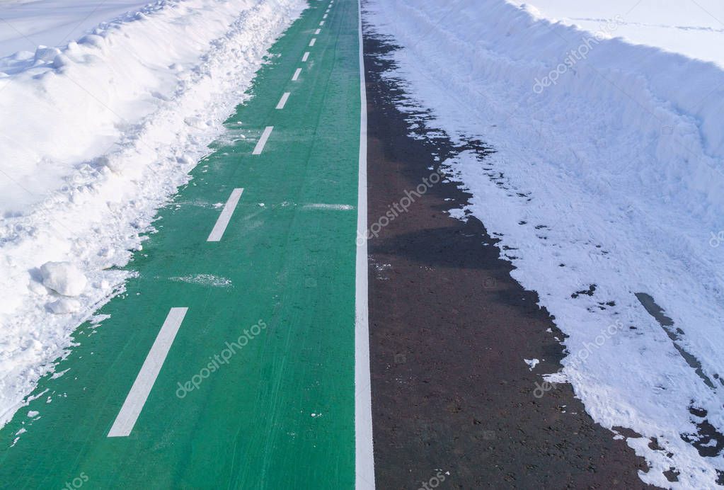 Empty bicycle path with marking line and coating of crumb rubber in winter between snowdrifts