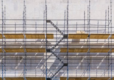 Ahşap döşemeleri ve bina duvarının yanındaki merdivenleri olan çok katlı bir iskele. Tamir işleri. Güneşli bir gün