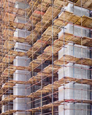 Yüksek beton kolonların etrafındaki ahşap döşemeli çok katlı iskeleler. İnşaat alanı, onarım