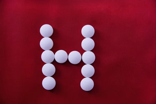 White round medical pills lie on a red background in the form of a letter H