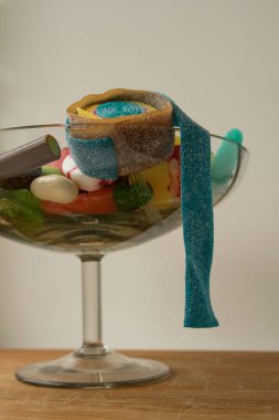 Değişik şekillerde çok renkli marmelat tatlısı cam bir vazonun içinde, beyaz arka planda tahta bir tahtanın üzerinde duruyor, kaba ve çarpık bir tatlılıkla.