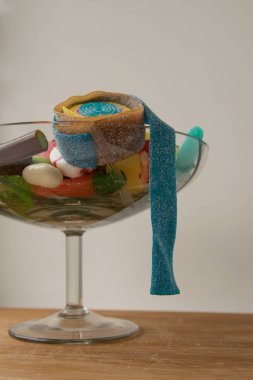 Değişik şekillerde çok renkli marmelat tatlısı cam bir vazonun içinde, beyaz arka planda tahta bir tahtanın üzerinde duruyor, kaba ve çarpık bir tatlılıkla.