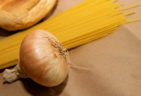 spaghetti, onions, bread and canned goods lie on a paper bag