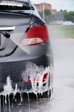 Araba yıkamada silah kullanmak gri bir arabanın farlarındaki deterjanı suyla yıkamak.