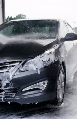 Deterjan gri bir arabanın önünde suyla yıkanmış.