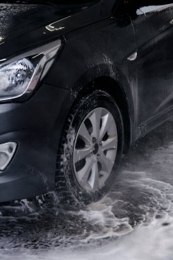 Oto yıkama ile, gri bir arabanın deterjanını suyla yıka.