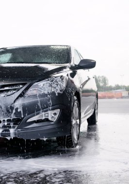 Deterjan gri bir arabanın önünde suyla yıkanmış.