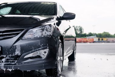 Deterjan gri bir arabanın önünde suyla yıkanmış.