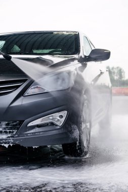 Deterjan gri bir arabanın önünde suyla yıkanmış.