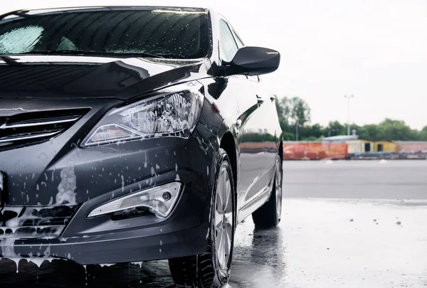 Deterjan gri bir arabanın önünde suyla yıkanmış.