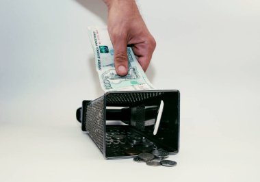 Erkeklerin elleri bir banknotu rendeleyiciye sürtüyor ve demir paralar aşağıda yatıyor.