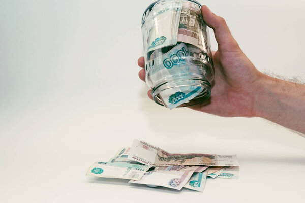 mans hand holds a glass jar filled with money and pops it out