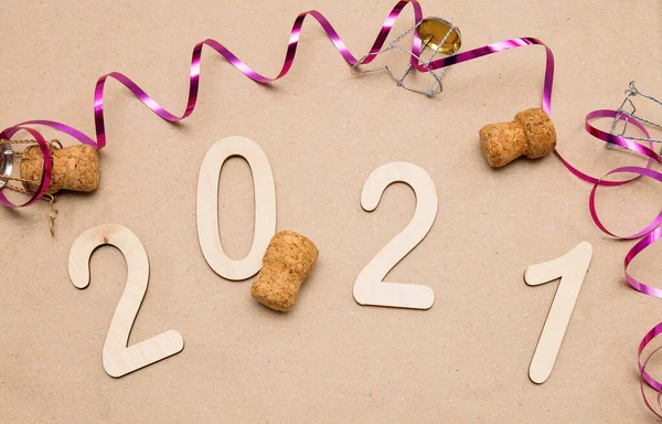 Light wooden 2021 numbers lie on craft paper with champagne corks, muzle and packing tape around